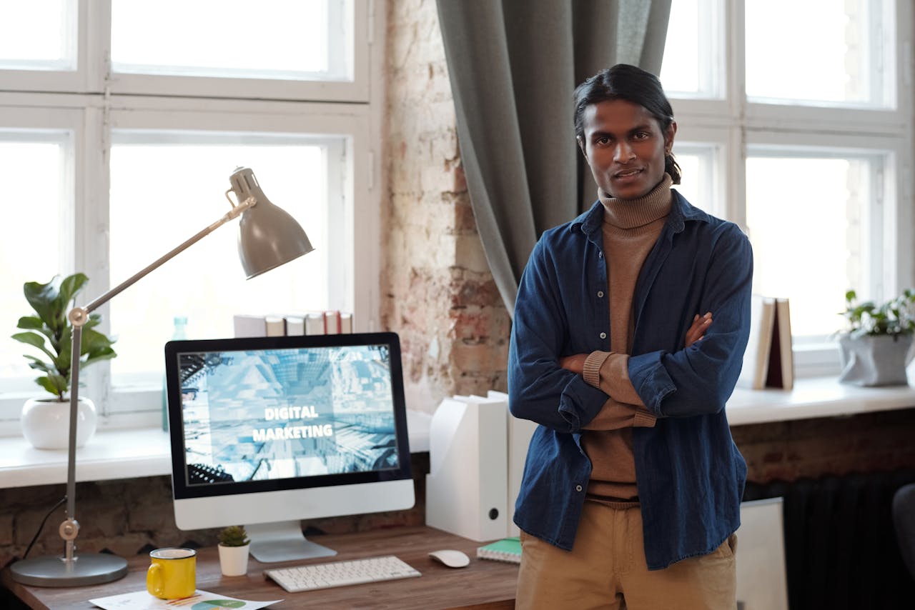 A man standing confidently in an office environment with digital marketing setup.
